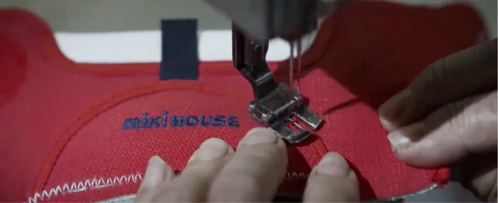 A craftsperson sewing the upper of a red MIKI HOUSE shoe