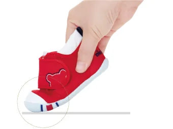 A hand flexing the forefoot of a red MIKI HOUSE shoe