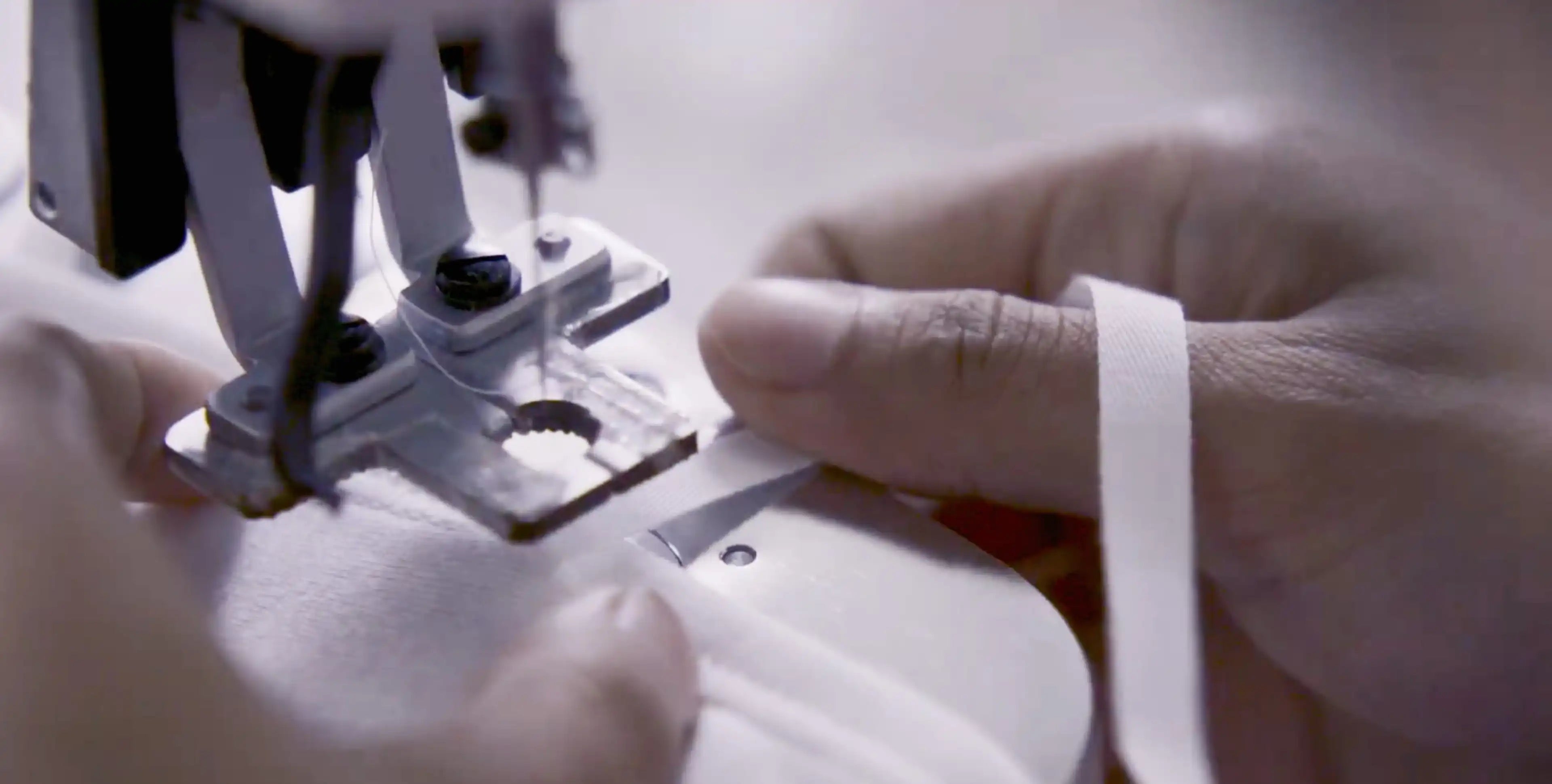 A craftsperson carefully guides white fabric through a sewing machine