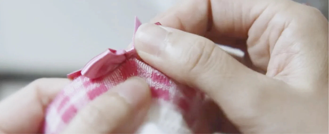 A small pink knitted sock is carefully finished by hand